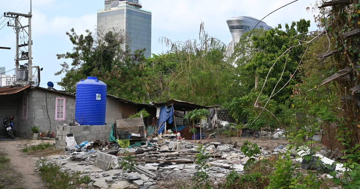 An informal settlement of makeshift dwellings on cleared ground, with high-rise towers of the formal city rising behind.